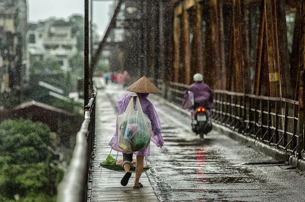 A person in a purple raincoat walking across a rain-soaked bridge